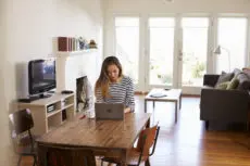 Woman Working From Home Using Laptop On Dining Table