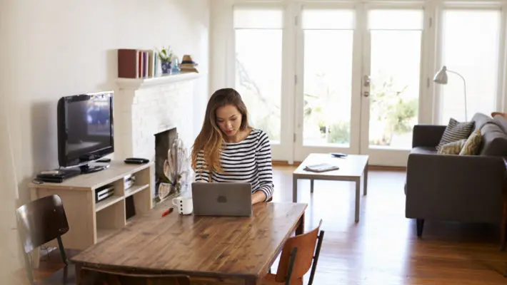 Woman Working From Home Using Laptop On Dining Table