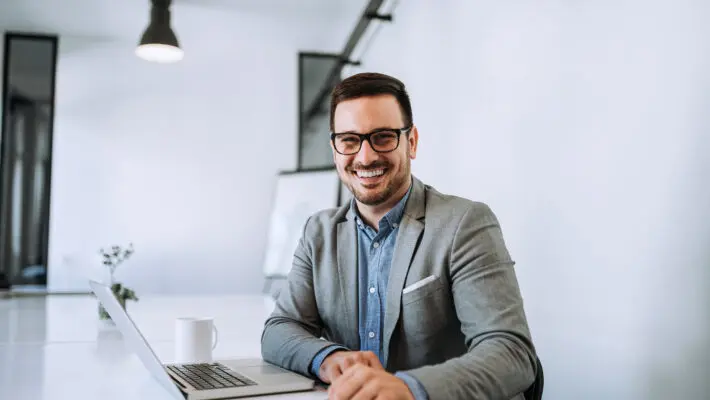 Young,Smiling,Entrepreneur,In,Bright,Office,Working,On,Laptop.