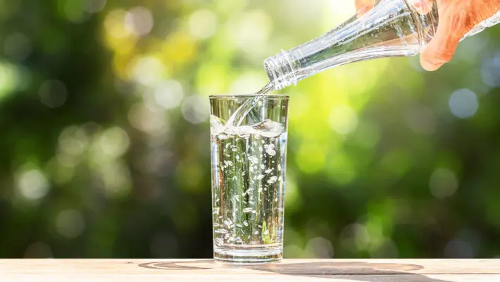 Hand,Holding,Drinking,Water,Bottle,Pouring,Into,Glass,On,Wooden