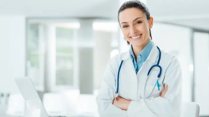 Confident,Female,Doctor,Sitting,At,Office,Desk,And,Smiling,At