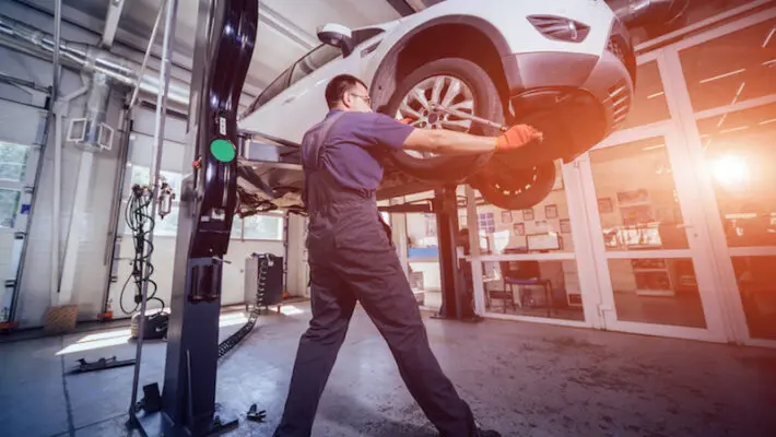 Car mechanic inspecting wheel and suspension detail of lifted automobile at repair service station