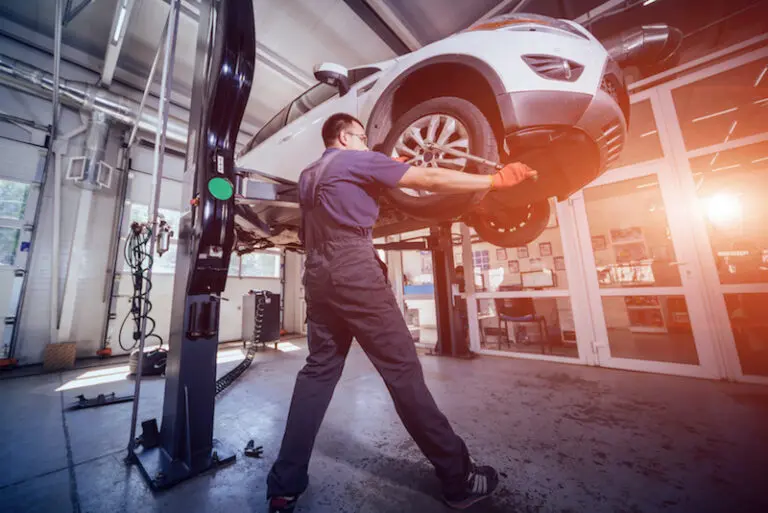 Car mechanic inspecting wheel and suspension detail of lifted automobile at repair service station