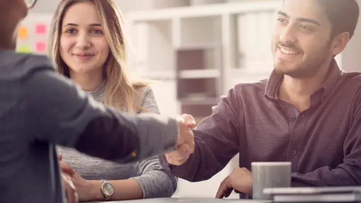 Young,Couple,Shaking,Hands,With,A,Female,Agent