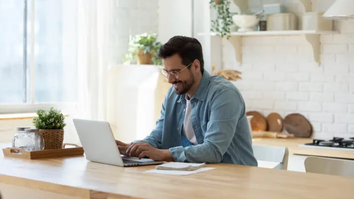 Smiling,Young,Man,Working,On,Laptop,In,Modern,Kitchen,,Checking