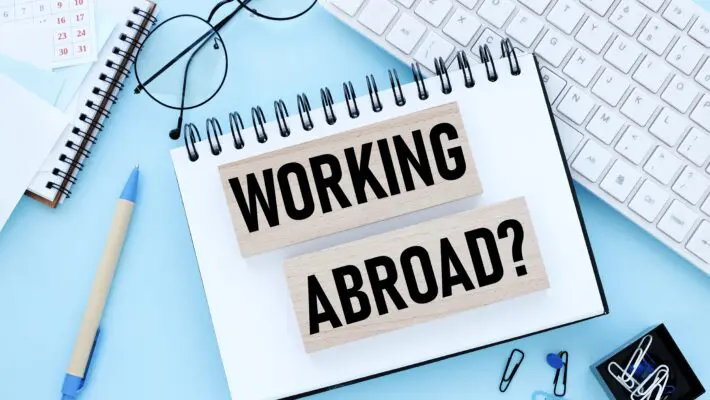Working,Abroad.,Text,On,Wooden,Blocks,On,A,Blue,Background.