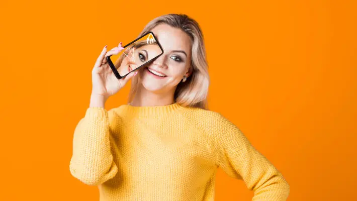 Cute,Young,Woman,In,A,Yellow,Sweater,Holding,A,Smartphone