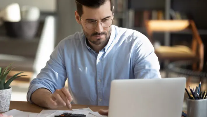 Focused,Young,Caucasian,Man,Look,At,Laptop,Screen,Calculate,Expenses