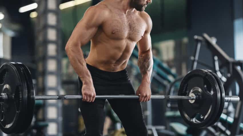 Strong man with naked muscular body exercising with heavy barbell