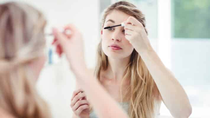 Young woman applying mascara while looking in mirror