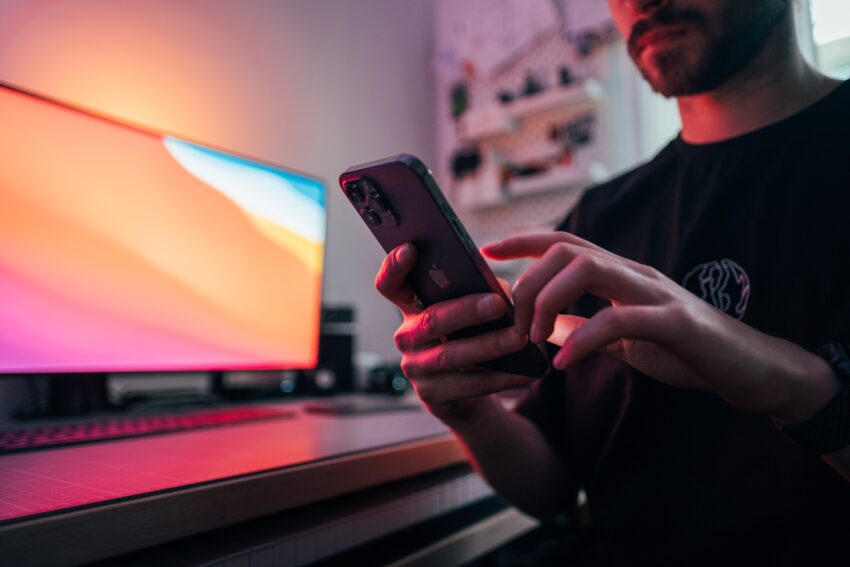 Man holding an iPhone in front of his desk, with a monitor in the background.